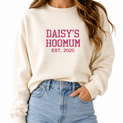 Person wearing a cream sweatshirt with 'DAISY'S HOOMUM EST. 2020' text and blue jeans on a white background