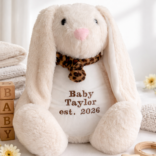 Plush bunny with personalized text on a white surface with baby-related items.